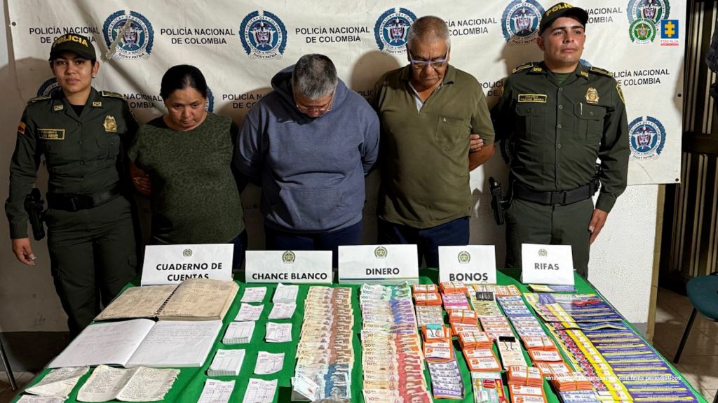 En la imagen aparecen los procesados, de frente, en medio de una pareja de servidores de la Policía Nacional. También, se observa el dinero en efectivo, 162 hojas de canche en blanco, 5.227 bonos y 1.700 boletas para rifas que fueron incautadas en diligencias de registro y allanamiento.