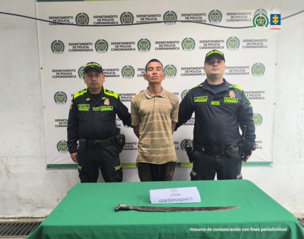 En la imagen aparece el procesado, de frente, en medio de una pareja de servidores de la Policía Nacional. También, se observa el machete que fue incautado durante el procedimiento de captura.