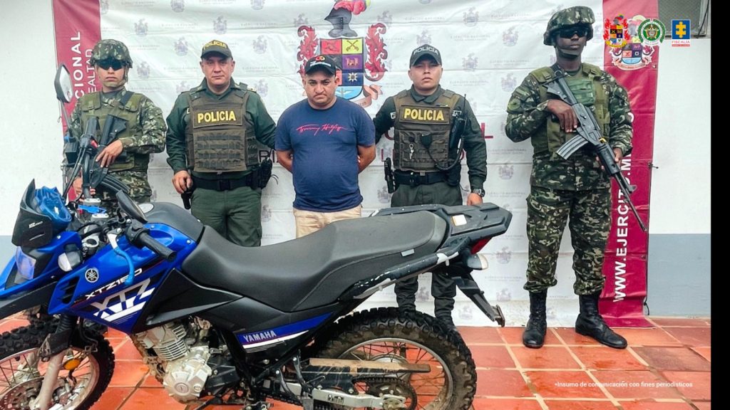 El procesado aparece rodeado y custodiado por uniformados armados del ejército y la Policía nacional, con sus manos esposadas a la espalda.