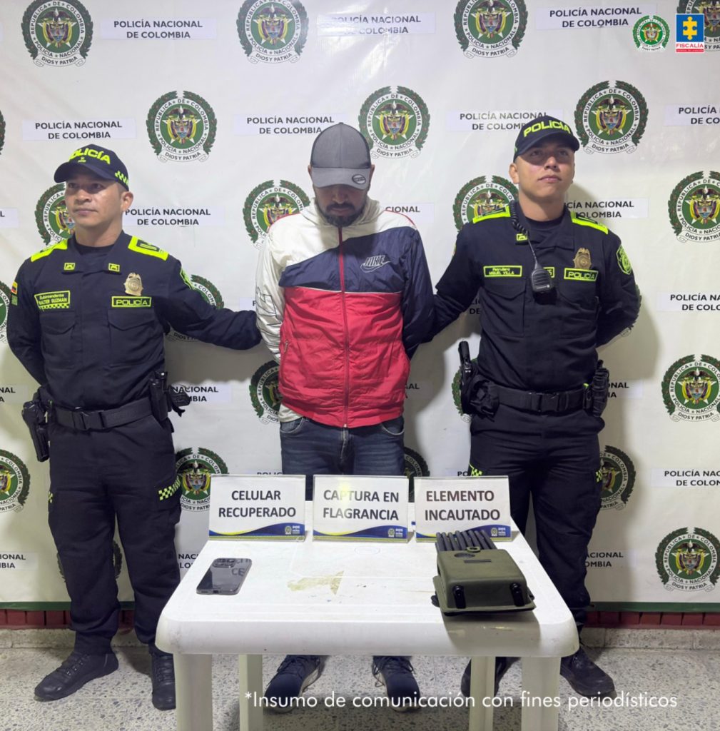 En la imagen aparece el capturado de frente, en medio de dos parejas de servidores de la Policía Nacional. También, se observan los elementos incautados durante la captura del procesado. 