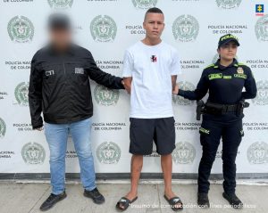 En la imagen se observa a un hombre esposado en el centro, custodiado por dos autoridades: a su izquierda, una persona con chaqueta negra que lleva las siglas "CTI" y "Policía Judicial" (con el rostro difuminado), y a su derecha, una mujer policía uniformada de la Policía Nacional de Colombia. El fondo es una pared con el escudo y el nombre de la Policía Nacional de Colombia repetidos, y en la esquina superior derecha aparece el logotipo de la Fiscalía General de la Nación. En la parte inferior se lee la frase "Insumo de comunicación con fines periodísticos".