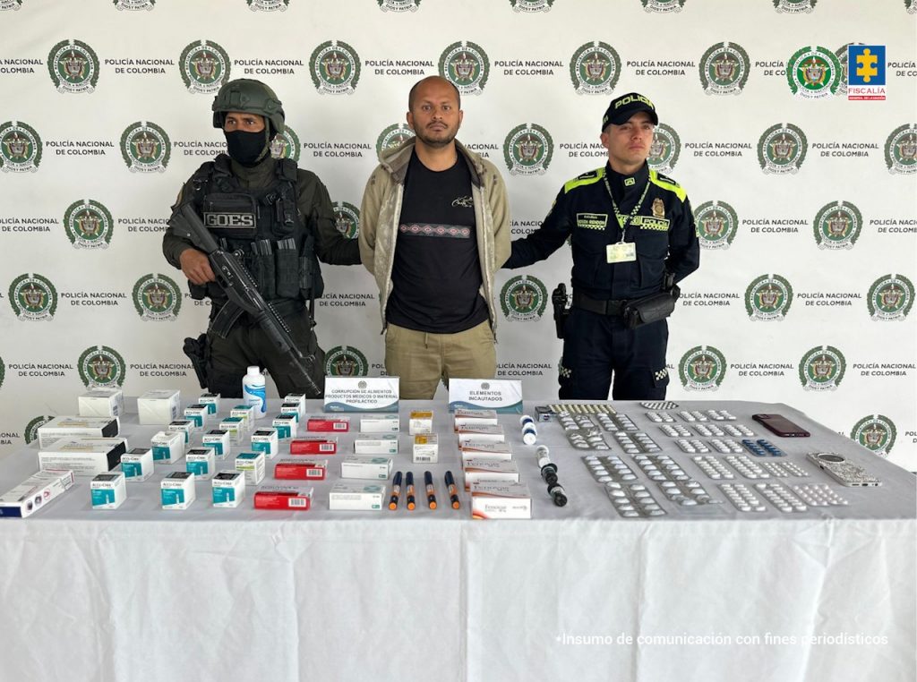 En la imagen aparece el judicializado de frente, en medio de una pareja de servidores de la Policía Nacional. También, se observan los medicamentos incautados durante el procedimiento de captura.