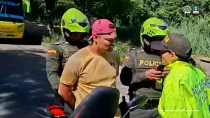 En la imagen se observa a un hombre con camiseta beige y gorra roja, que está siendo retenido por la Policía Nacional de Colombia. Tiene las manos hacia atrás, aparentemente esposadas.Alrededor de él hay al menos tres uniformados de la Policía: dos con casco verde fluorescente y chaleco antibalas, y otro con chaqueta amarilla que parece estar hablando con el detenido. En el fondo se ve un bus de transporte público y vegetación a un costado de la vía. En la parte superior derecha aparecen los logos de la Policía Nacional de Colombia y la Fiscalía General de la Nación, y abajo a la derecha la leyenda: “Insumo de comunicación con fines periodísticos”.