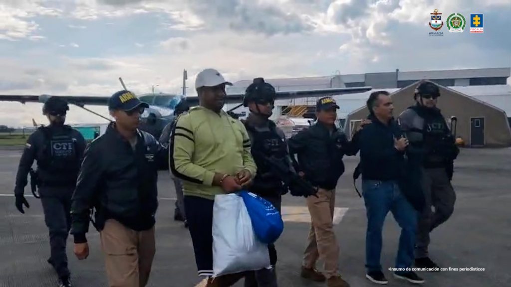 En una plataforma aeroportuaria, varios funcionarios del CTI caminan escoltando a dos hombres esposados. Al fondo se observa una avioneta de hélice, una carpa y edificios aeroportuarios; en la esquina superior derecha aparecen logotipos institucionales y en la parte inferior derecha una marca de agua que dice "Insumo de comunicación con fines periodísticos".