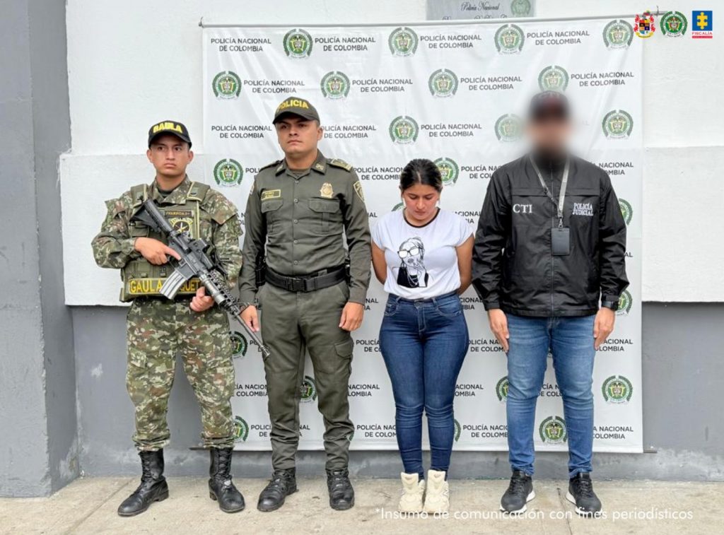 En la imagen se ve una mujer detenida bajo custodia de un investigador del CTI, un integrante del Ejército y de la Policía Nacional. Detrás, un backing institucional.