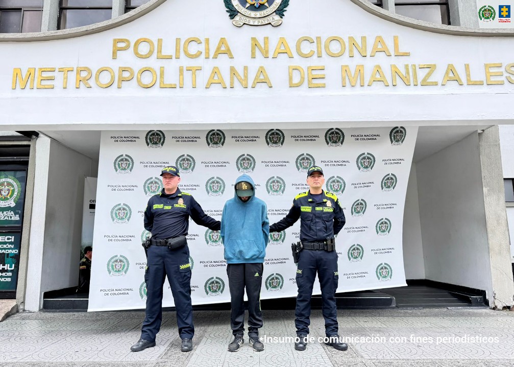 En la foto está el capturado con dos policías a los lados y al fondo el pendón con logos de la Fiscalía.