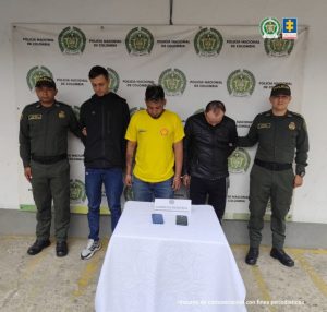 En la imagen se observa, en medio de dos integrantes de la Policía Nacional, a tres procesados de frente. También, se evidencian los elementos incautados en las diligencias de allanamiento y registro.