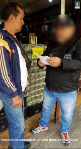 En esta imagen se observa a dos hombres de pie frente a un establecimiento comercial, probablemente una tienda o mercado.Uno de ellos, a la izquierda, viste ropa casual (chaqueta deportiva azul con franjas, camiseta blanca y jeans) y parece ser el propietario o encargado del lugar. El otro, a la derecha, lleva una chaqueta del CTI con la inscripción “Policía Judicial” y una gorra del mismo organismo. Sostiene unos documentos que parece estar mostrando o leyendo al otro hombre. Detrás de ellos se ven productos apilados y un cartel que dice “Paco litro $4.000”, lo que refuerza que la escena ocurre en un entorno comercial. En la esquina superior derecha aparece el logo de la Fiscalía General de la Nación de Colombia, y en la parte inferior se lee: “Insumo de comunicación con fines periodísticos”.