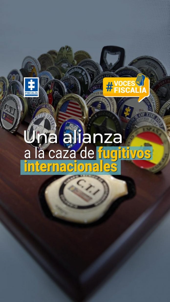 La imagen muestra una colección de insignias y medallas de distintas agencias de seguridad y justicia, entre ellas algunas con banderas de diferentes países. En primer plano se distingue una placa del C.T.I. (Cuerpo Técnico de Investigación) de la Fiscalía General de la Nación de Colombia. En la parte superior izquierda aparece el logo de la Fiscalía, y en la parte derecha, un sello amarillo con el texto #VocesFiscalía. Sobre la imagen, en el centro, se lee el texto principal: “Una alianza a la caza de fugitivos internacionales”, con las palabras “fugitivos internacionales” destacadas en color amarillo y azul.
