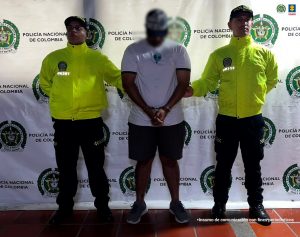 En la imagen se observa a un hombre esposado, custodiado por dos agentes de la Policía Nacional de Colombia, quienes visten uniformes de color amarillo con distintivos institucionales. Al fondo hay un pendón con los logos de la Policía Nacional y la Fiscalía General de la Nación, lo que indica que se trata de una captura oficial.El texto en la parte inferior derecha señala que se trata de un “insumo de comunicación con fines periodísticos”, lo cual sugiere que la imagen fue difundida por las autoridades como parte de un comunicado o boletín informativo sobre la aprehensión del individuo.