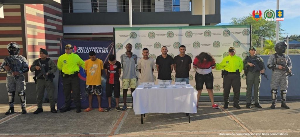Los capturados aparecen esposados y custodiados por uniformados de lña FAC, Policía nacional y en una mesa los elementos incautados.