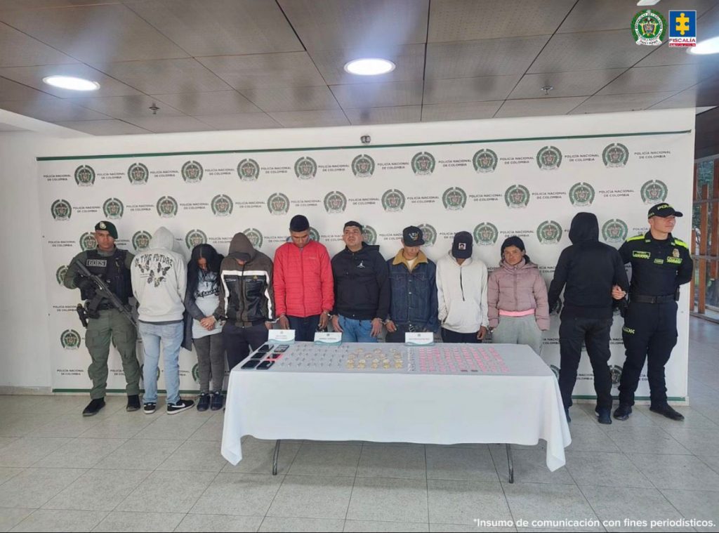 Nueve personas capturadas aparecen de pie junto a dos uniformados de la Policía. Detrás de ellos se observa un panel institucional con los logos de la Policía Nacional. Todos están alineados frente a la cámara en un espacio cerrado.