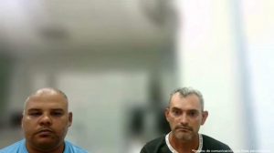 La imagen muestra un encuadre frontal de dos personas ubicadas una al lado de la otra, ocupando la parte inferior de la composición.Contexto general: El fondo está desenfocado (efecto de profundidad de campo), lo que sugiere un espacio interior amplio, posiblemente una sala institucional o un edificio con paredes claras y elementos verticales. La iluminación es uniforme y suave, sin sombras fuertes. Elementos en primer plano: A la izquierda aparece una persona con la cabeza rapada o con cabello muy corto. Lleva una camiseta de color azul claro. Está situada más cerca de la cámara que el fondo, y su rostro está centrado dentro de su mitad de la imagen. A la derecha aparece otra persona con cabello corto de color oscuro con canas visibles. Lleva una prenda de color oscuro (posiblemente verde o negro) con un borde claro en el cuello. Esta persona también mira hacia la cámara, con el rostro bien enfocado. Ambas personas están posicionadas de frente, mirando directamente al lente, con postura erguida. No hay interacción visible entre ellas ni objetos adicionales en primer plano. Fondo: El fondo presenta tonos claros (blancos y grises), con formas verticales que podrían ser columnas, marcos o paredes internas. Debido al desenfoque, no se distinguen detalles precisos de los objetos o el lugar. Texto visible: En la esquina inferior derecha se alcanza a leer un texto pequeño en blanco que dice: “*Insumo de comunicación con fines periodísticos.”