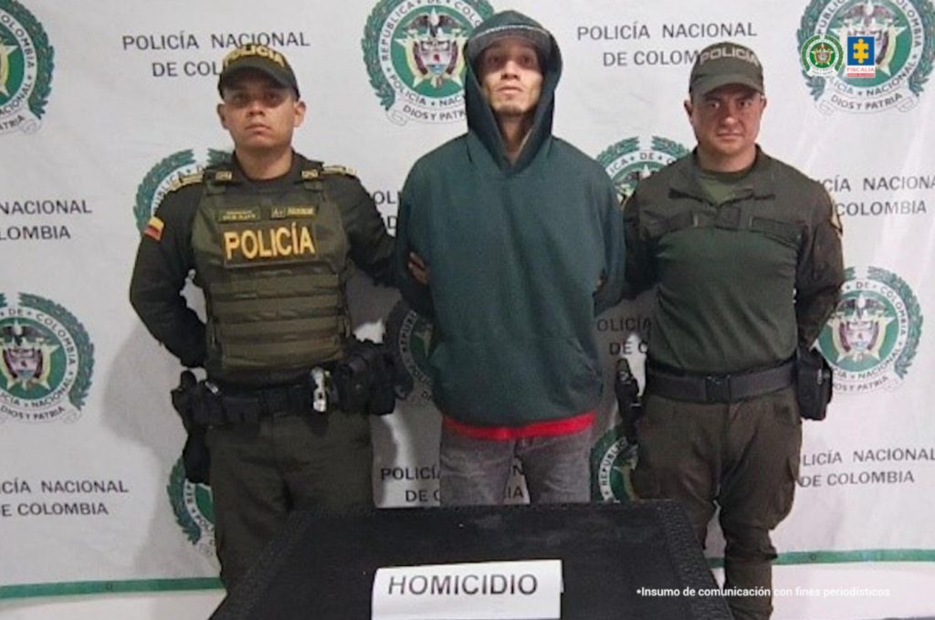 En la fotografía se aprecia de pie y con los brazos atrás a Wilder Andrés Grajales Giraldo. Viste con buso de capucha de color verde oscuro y ribete rojo en la parte de abajo; así como pantalón gris. En sus extremos hay uniformados de la Policía Nacional. Delante de ellos hay una superficie color marrón y sobre ella hay un letrero que dice: ‘Homicidio’. Detrás de ellos hay un pedón institucional de la Policía.