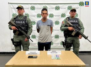 En la imagen está el presunto victimario con dos servidores del Gaula de la Policía Nacional y el celular incautado en una mesa