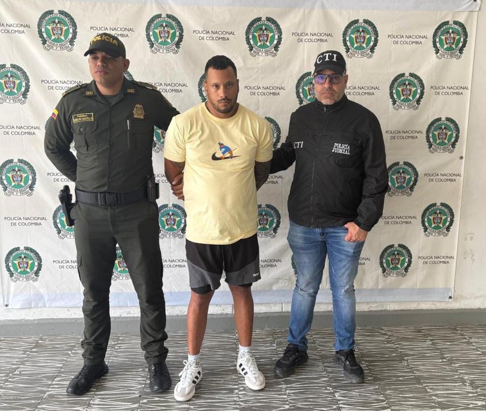 En la fotografía aparece de pie y con los brazos atrás William Andrés Lenis Ortiz. Viste con camiseta de mangas cortas, color amarillo, con estampado a la altura del pecho; bermuda de colores negro y gris y zapatillas blancas. A su extremo izquierdo hay un servidor del CTI de la Fiscalía y al derecho un uniformado de la Policía Nacional. Detrás de ellos hay un pendón institucional de la Policía.