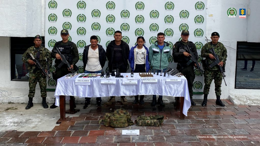 Se visualiza a los cuatro procesados junto a uniformados de la Policía y Ejército Nacional. Detrás de ellos el banner que identifica a la Policía Nacional.