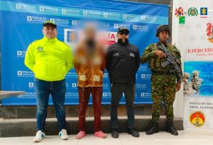 Se visualiza al capturado con el rostro difuminado, Detrás de ellos se ubican los banners institucionales de la Fiscalía General de la Nación y Ejército Nacional.
