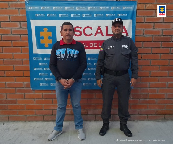 En la fotografía aparece un capturado junto a personal de Fiscalía General de la Nación. En la parte posterior de la imagen se ve un banner de la Fiscalía General de la Nación.      