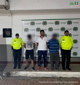 capturado de frente custodiado por dos policías. Detrás banner de la Policía Nacional.