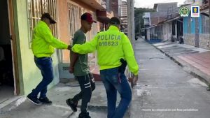 En la fotografía se aprecia a Wilmer Alexis Molina Patiño, alias Mexicano, con los brazos atrás y esposado, en acción de caminata y saliendo de una vivienda hacia una vía. Viste camiseta de manga corta color verde; pantalón de sudadera oscuro con rayas blancas horizontales a la altura del muslo; zapatillas oscuras y gorra roja. A lado y lado de él hay dos uniformados de la Policía Nacional.