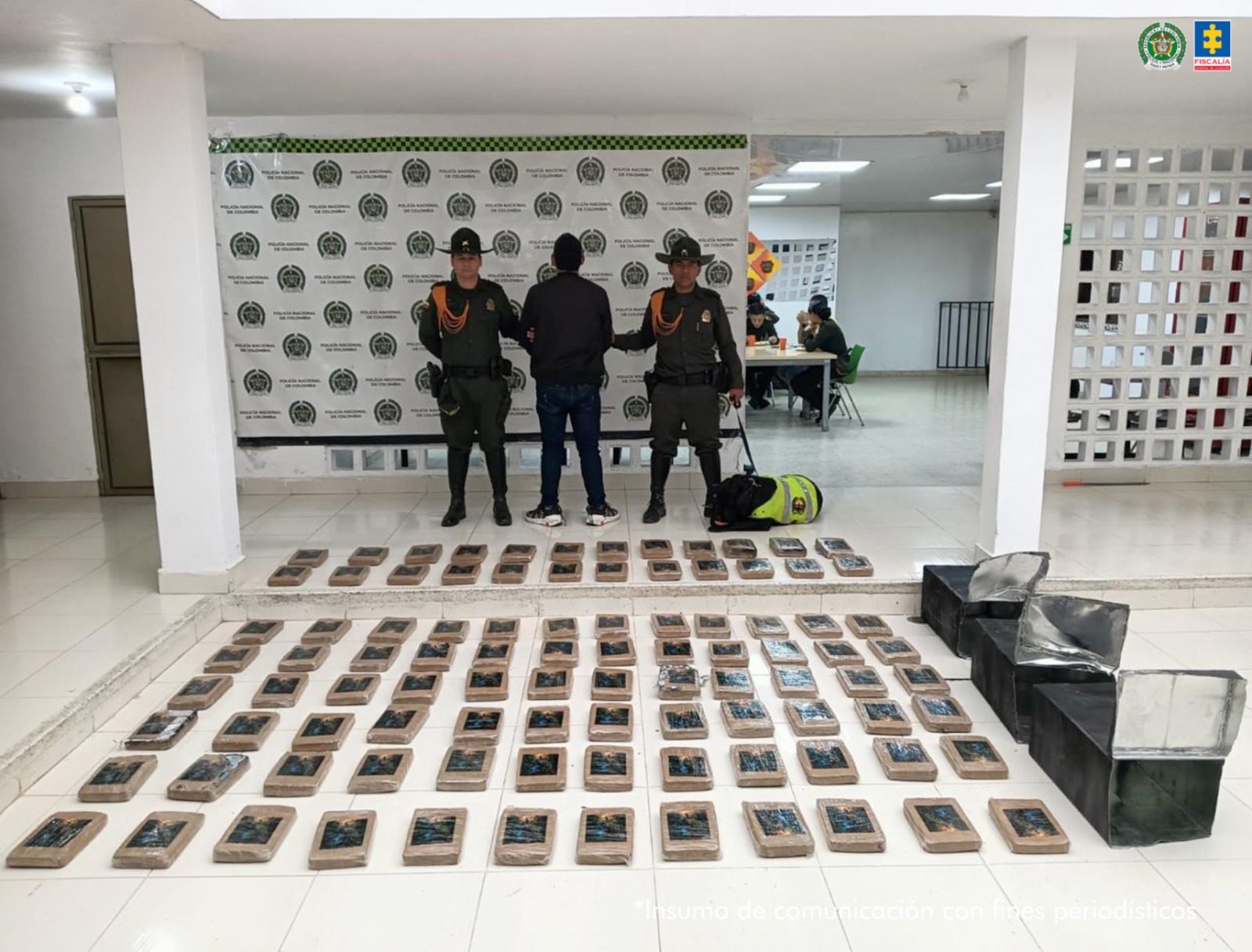 El capturado se encuentra de espalda y custodiado por dos uniformados de la Policía de Carabineros y Protección Ambiental . Detrás se observa el backing de la Policía Nacional y se observa en el piso todos los paquetes de marihuana que venian camuflados dentro de las tres cajas metálicas de color negro.