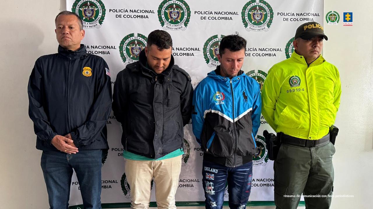 Los capturados aparecen de pie, con las manos esposadas en la espalda, frente a un banner de la Policía. A cada lado tienen miembros de la Fuerza Pública.