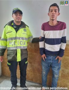 el hombre de nacionalidad extranjera viste saco de rallas blancas y rojas y está acompañado de un policía.