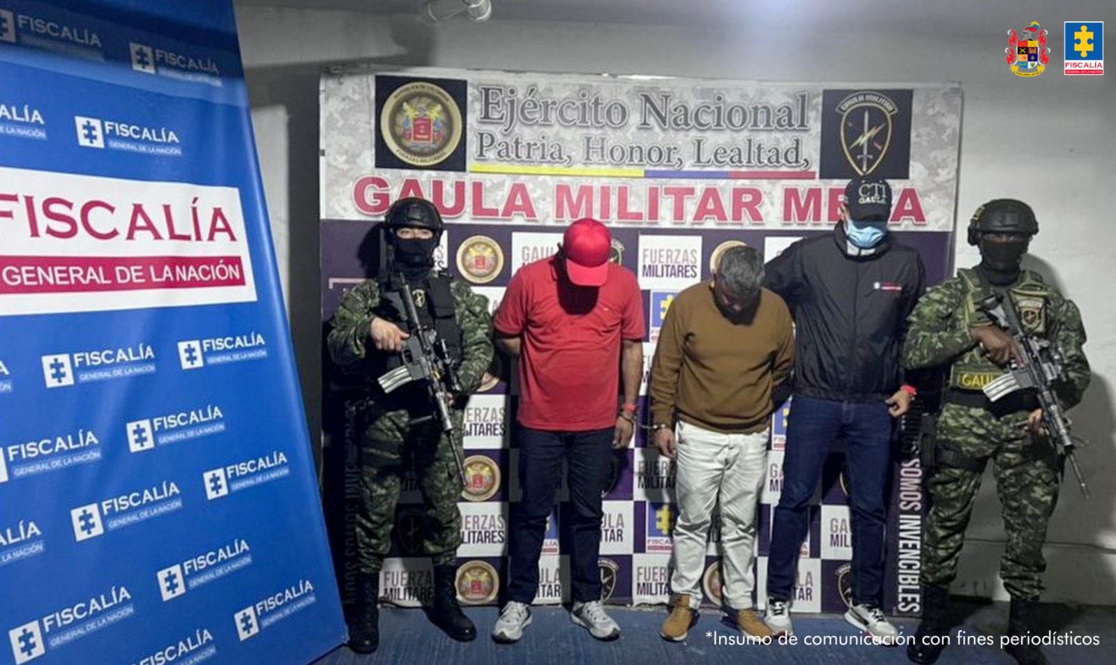 capturados con gorra y cabeza agachada custodiados por investigador del CTI de la Fiscalía y militares del Ejército Nacional. Detrás banner de la Fiscalía y del grupo Gaula Militar.