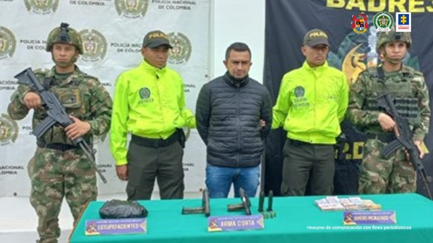 En la fotografía aparece el capturado en medio de dos uniformados de la Policía Nacional y dos del Ejército Nacional. Al frente de ellos una mesa con el material incautado (sustancias estupefacientes, armas y munición). En la parte posterior se observa banner de la Policía y Ejército Nacional