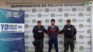 capturado de frente custodiado por dos policías, detrás banner de la Policía Nacional.