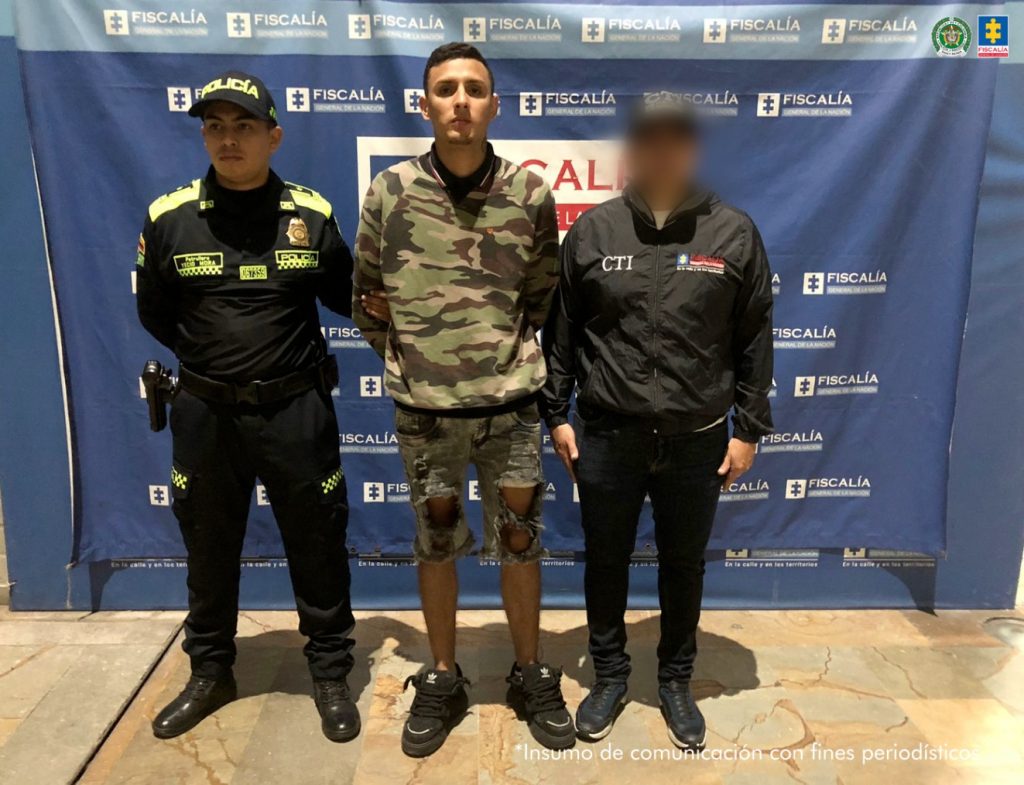 En la fotografía está el procesado en medio de un servidor del CTI y otro de la Policía Nacional y detrás un pendón de la Fiscalía General de la Nación