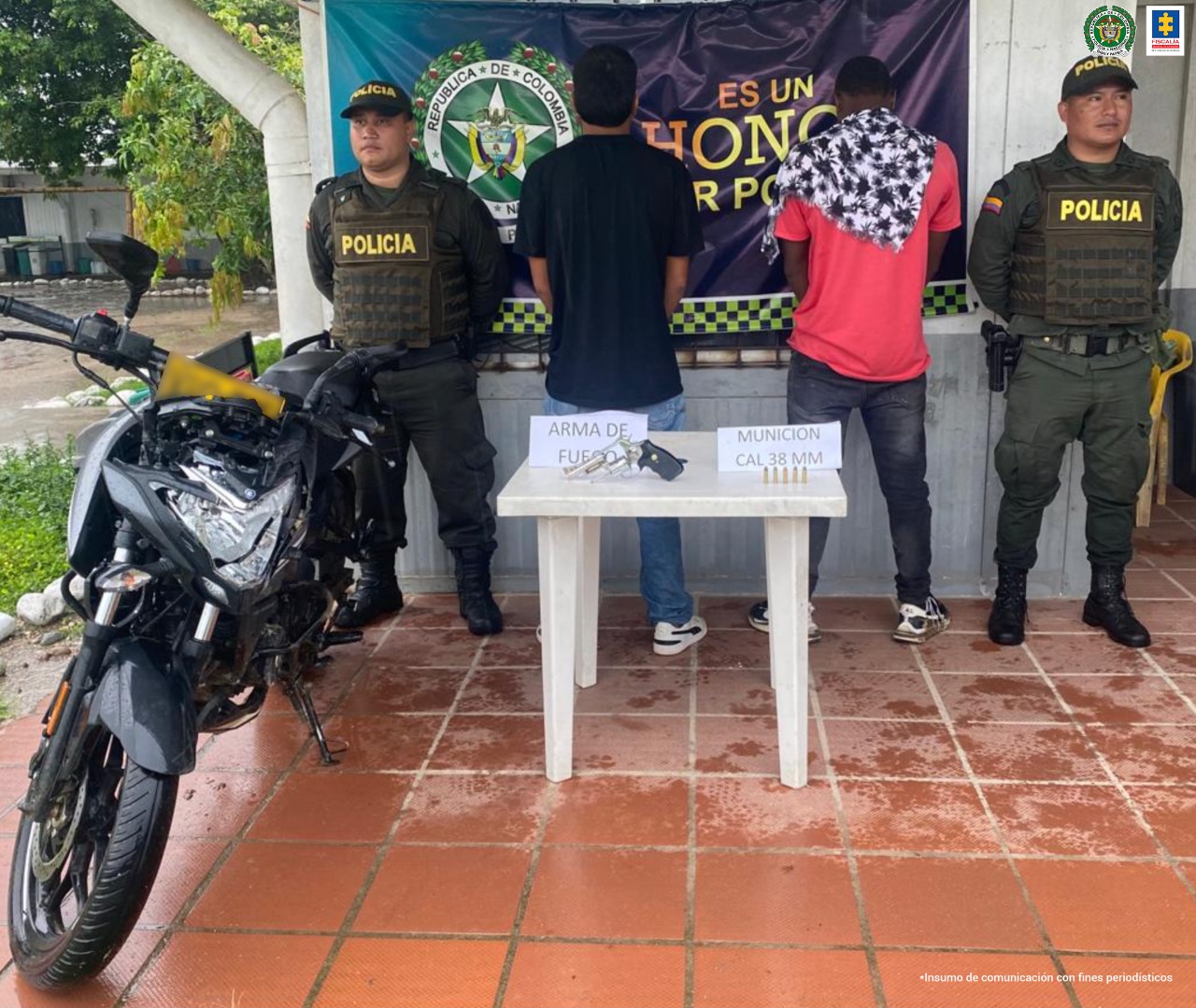 En la fotografía aparecen dos capturados, junto a personal de Policía Nacional y Fiscalía General de la Nación. En la parte posterior de la imagen se ven banners de Policía Nacional y la Fiscalía General de la Nación.