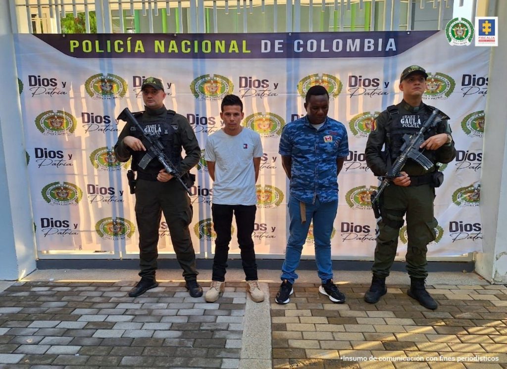capturados de frentre custodiados por un militar y un policía. de5trás banner del Gaula Militar Ariari.