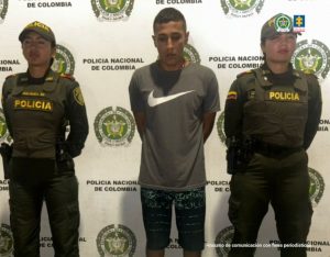 En la fotografía aparece de pie y con los brazos atrás Yerson Duván Garzón Campo. Viste con camiseta, de mangas cortas y de color verde oliva; así como bermudas ngras desgastadas. En sus extremos hay uniformados de la Policía Nacional. Detrás de ellos hay un pendón institucional de la Policía.