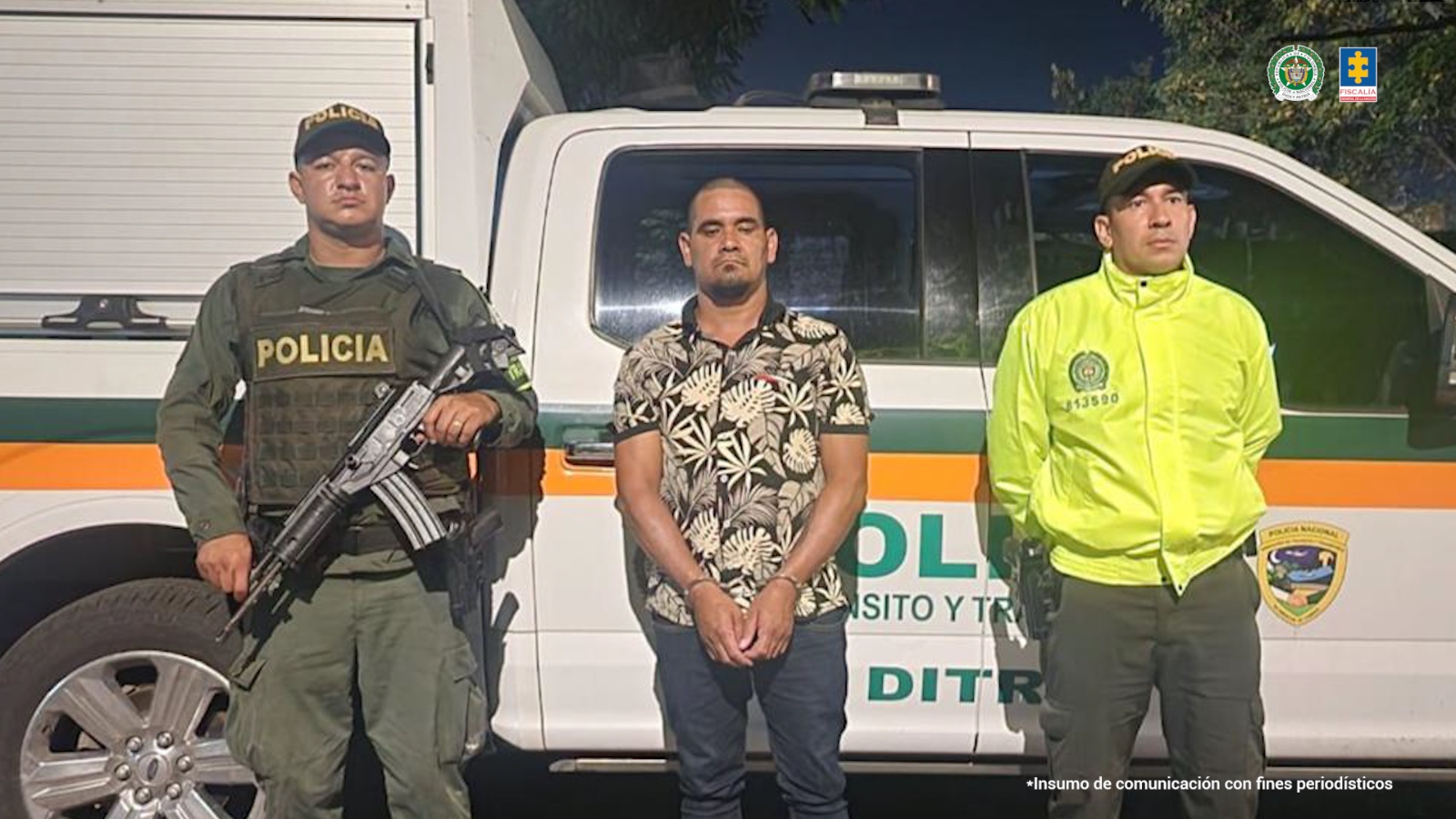 En la fotografía aparece el capturado en el centro, con dos miembros de la policía a sus costados. En la parte trasera aparece un carro de la Policía.