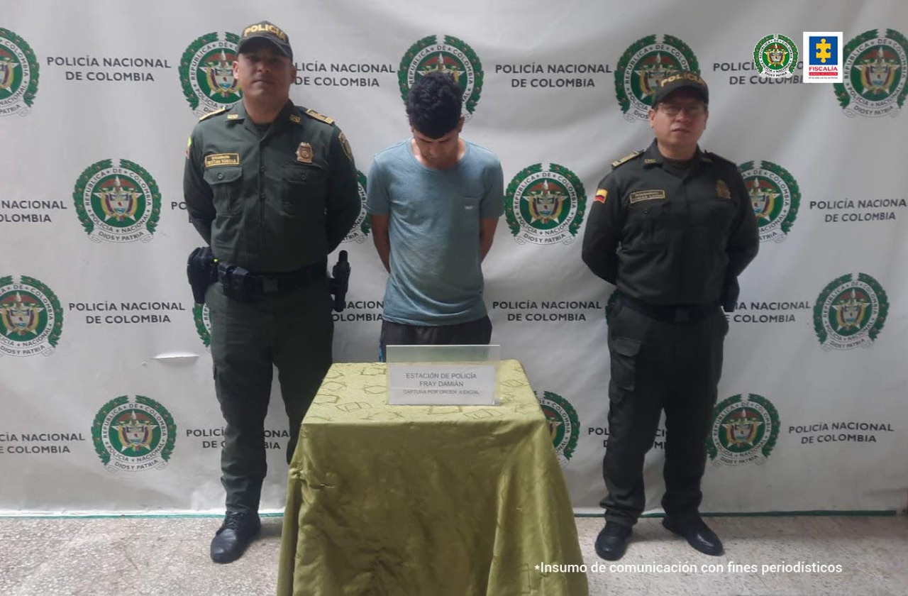 En la fotografía aparece un hombre capturado, junto a dos agentes de la Policía Nacional. En la parte posterior de la imagen se ve un banner de la Policía Nacional