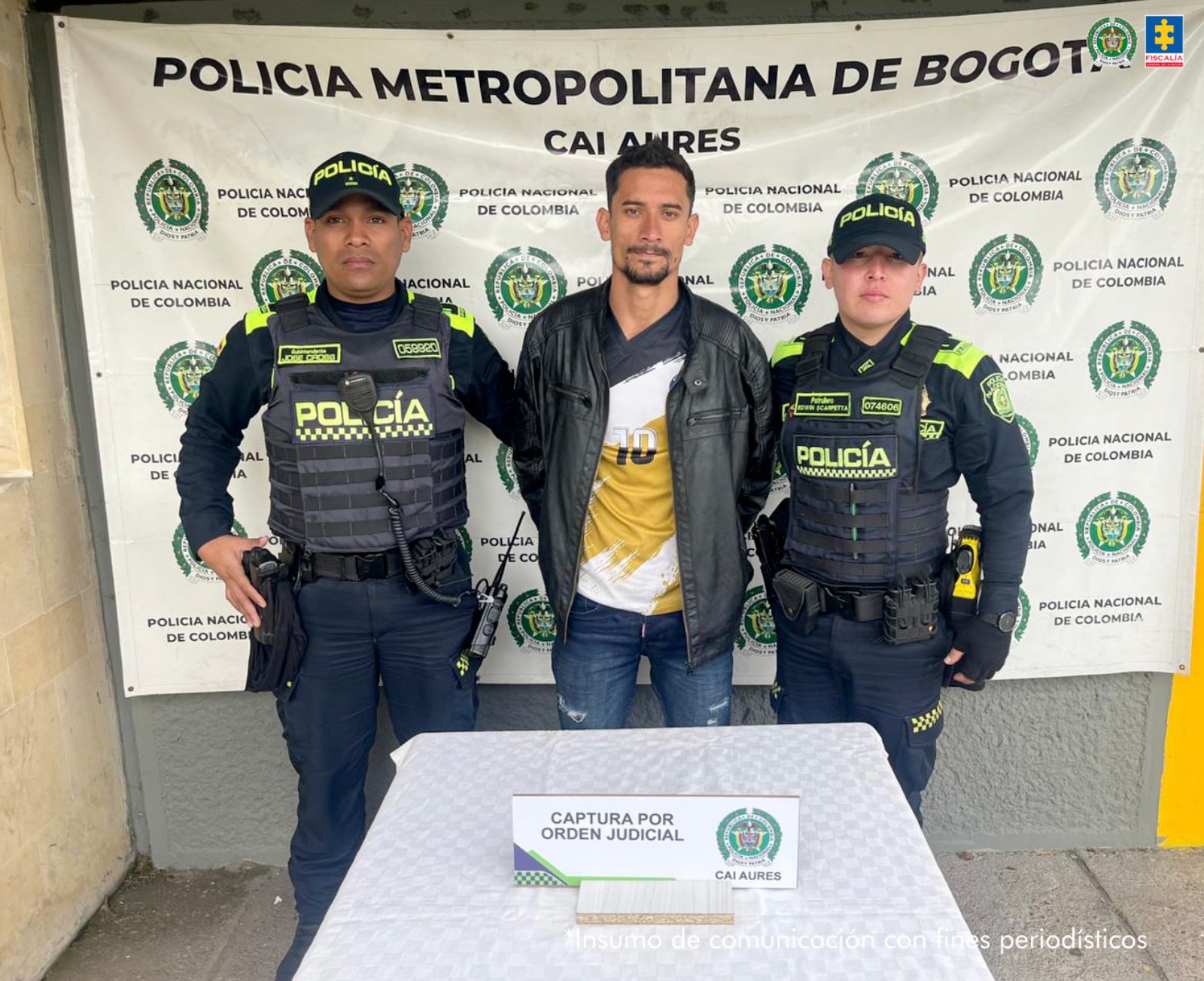 Se visualiza al capturado junto a dos uniformados de la Policía Nacional. Detrás el banner que identifica a la Policía Metropolitana de Bogotá.