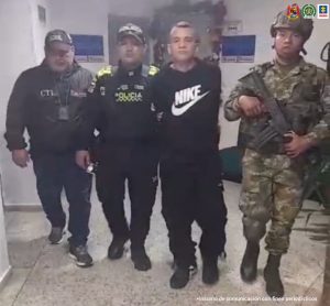 En la foto se aprecia en acción de caminata, por pasillo, a Yojan Abel Rodríguez Duarte. Viste con camiseta de manga corta negra con estampado blanco a la altura del pecho con la palabra ‘Nike’ y el símbolo correspondiente; pantalón y zapatos negros. Al lado derecho de él hay un servidor del CTI de la Fiscalía y un uniformado de la Policía Nacional. Al lado izquierdo un uniformado del Ejército.