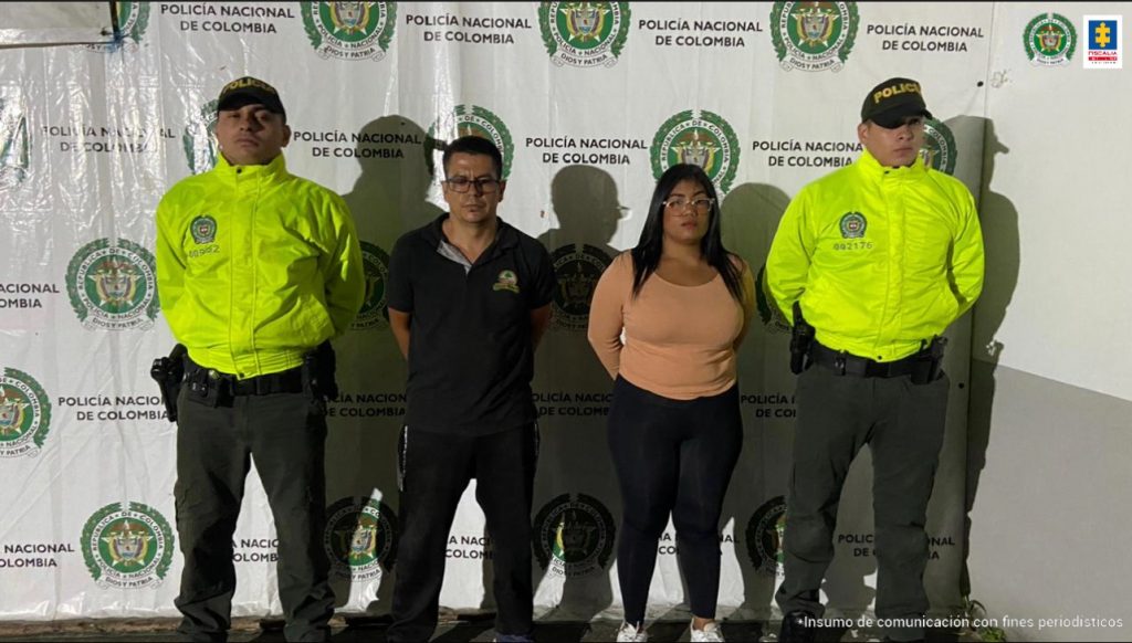 En la foto aparecen de pies y con los brazos atrás Yon Alexánder Álvarez Rodríguez, alias Pollo, y Nazareth José León Rodríguez. El hombre viste pantalón y camiseta de manga corta y cuello color negro, usa lentes. La mujer viste con blusa de manga larga color salmón y pantalón negro al cuerpo; usa lentes y tiene el cabello largo. A lado y lado de ellos hay uniformados de la Policía Nacional y detrás de ellos hay un pendón de la Policía.