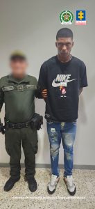 En la fotografía se aprecia de pie y con los brazos atrás a Yordan David Paz Lucumí. Viste camiseta de manga corta y de color negro, con la palabra ‘Nike’, en blanco, a la altura del pecho; asimismo, jean azul claro desgastado y zapatillas blancas. A su lado derecho hay un uniformado de la Policía Nacional.