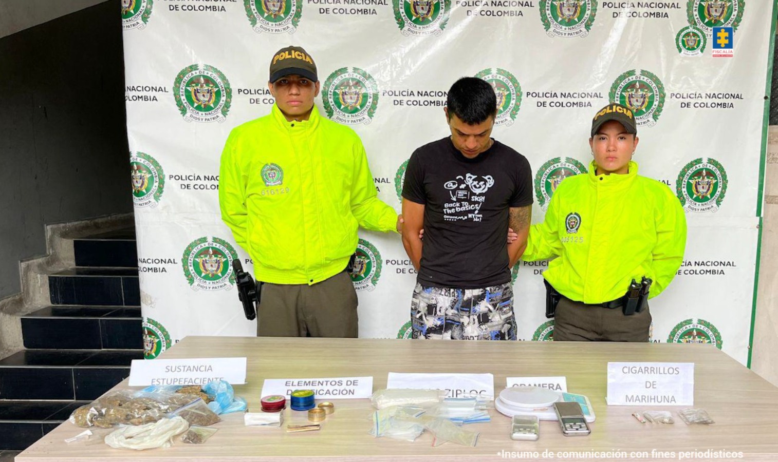 el capturado de frente custodiado por dos policías. Delante una mesa con material incautado. Detrás banner de la Policía Nacional.