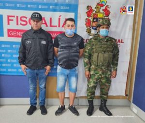 En la imagen se ve una persona detenida bajo custodia de un integrante del CTI de la Fiscalía y del Ejército. Detrás suyo backings institucionales.