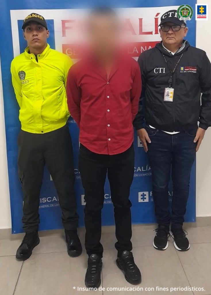 En la fotografía se observa el capturado en medio de Investigador del CTI y uno de la Policía Nacional. En la parte posterior se aprecian los banners de la Fiscalía y Policía Nacional