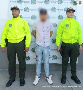 En la imagen se ve una persona detenida bajo custodia de dos integrantes de la Policía Nacional.