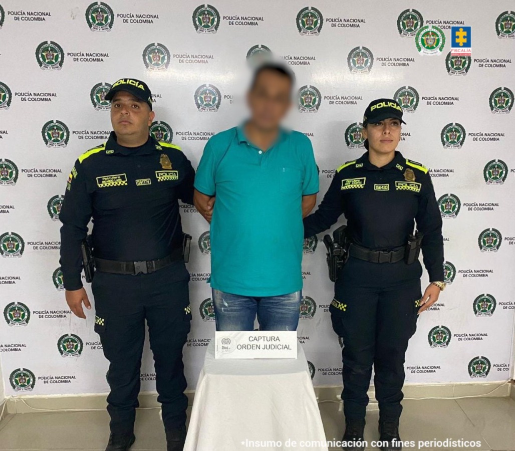 En la imagen se ve una persona detenida bajo custodia de dos integrantes de la Policía Nacional.