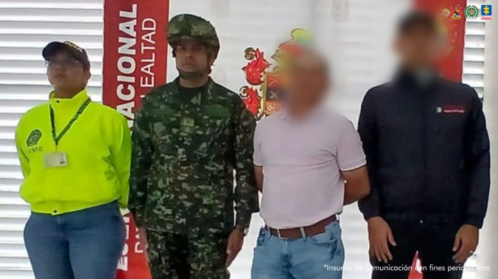 en la imagen se ve una persona detenida bajo custodia de un servidor del CTI, Policía y Ejército. Detrás suyo backings institucionales.