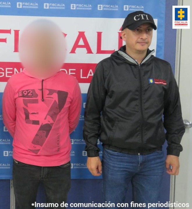 En la imagen se ve un hombre detenido custodiado por un investigador del CTI. Detrás suyo un backing de la Fiscalía.