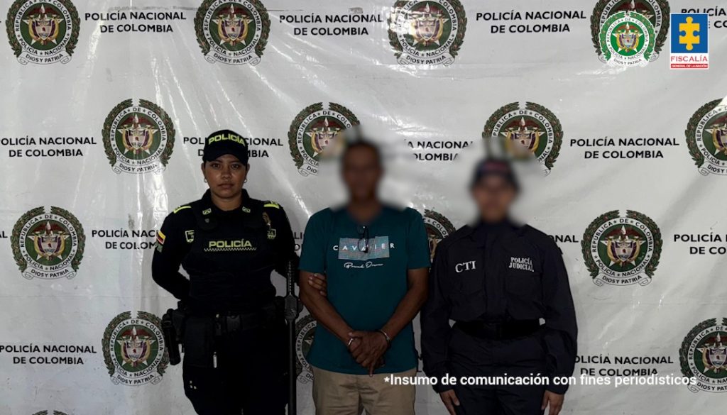 en la imagen se ve una persona detenida bajo custodia de un investigador del CTI y un uniformado de la Policía Nacional. Detrás suyo, un backing institucional.