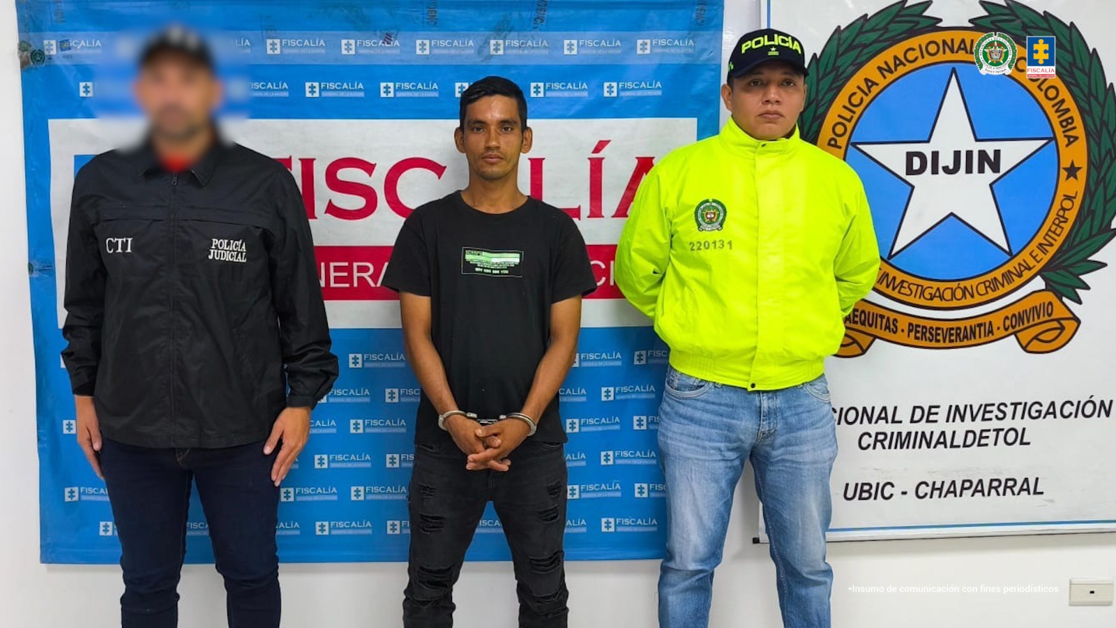En la imagen se ve una persona detenida bajo custodia de dos integrantes de la Policía Nacional. Detrás suyo backings institucionales.